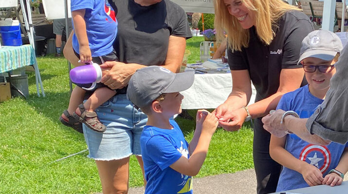 Excellus BlueCross BlueShield Utica Regional President Eve Van de Wal gives Power of Produce Kids Club tokens to the Townsend family (Michelle, Vance, Everett, and Maverick) at the Clinton Farmers Market.